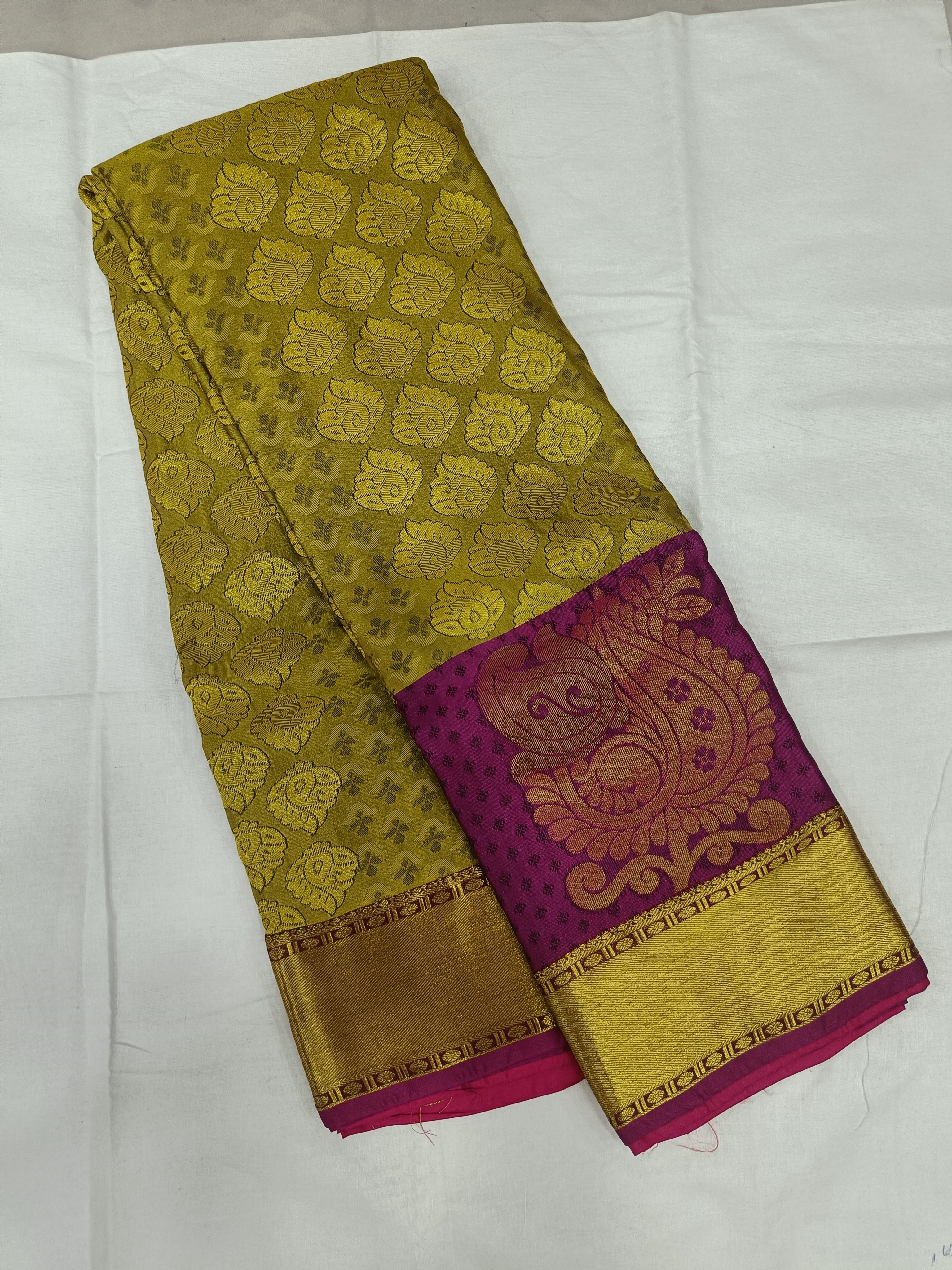 Olive-gold silk saree folded, purple pallu panel with ornate motifs and border