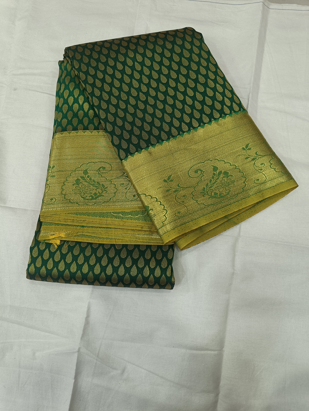 Folded dark green saree with dotted geometric pattern and gold zari border