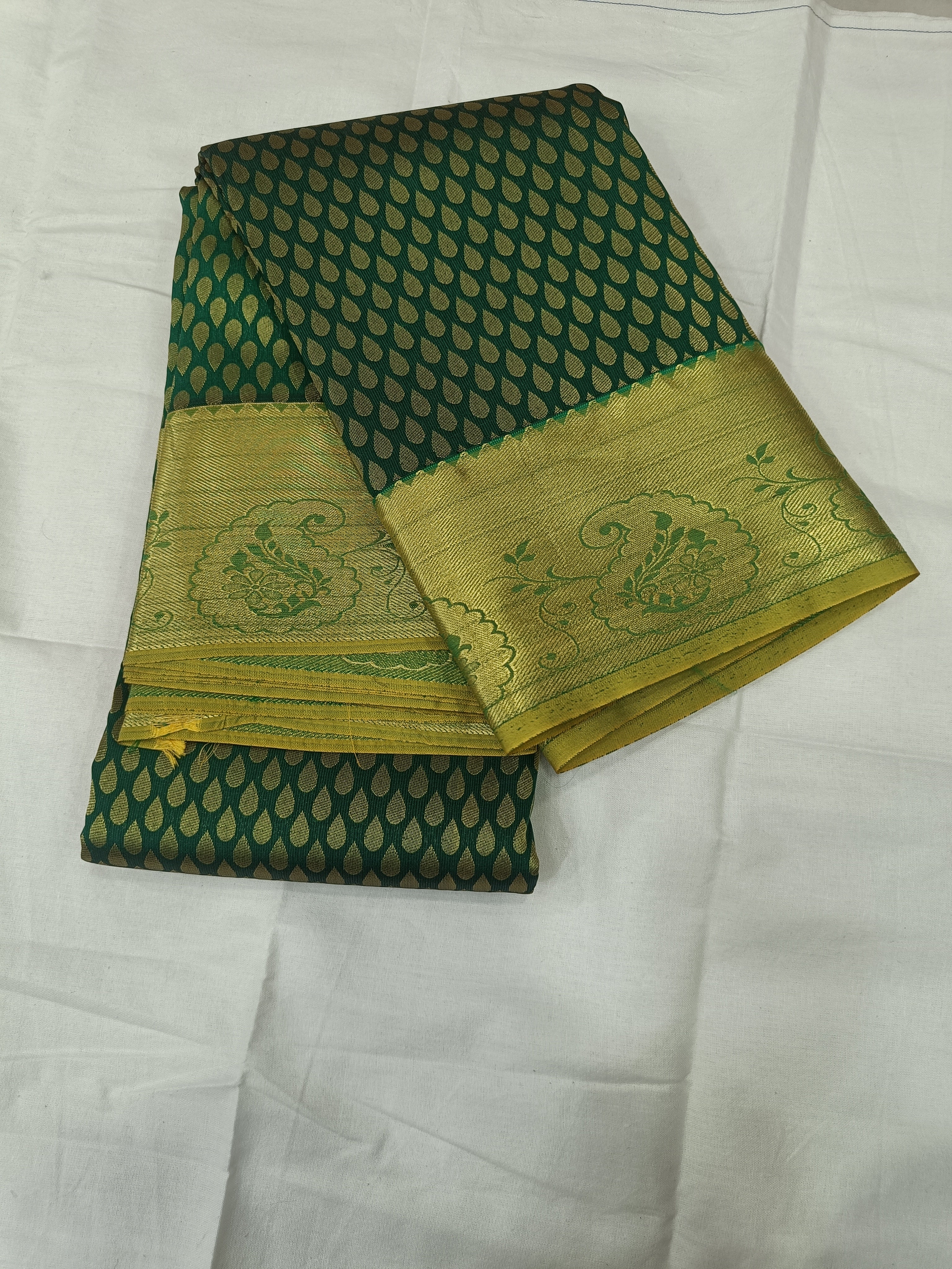 Folded dark green saree with dotted geometric pattern and gold zari border