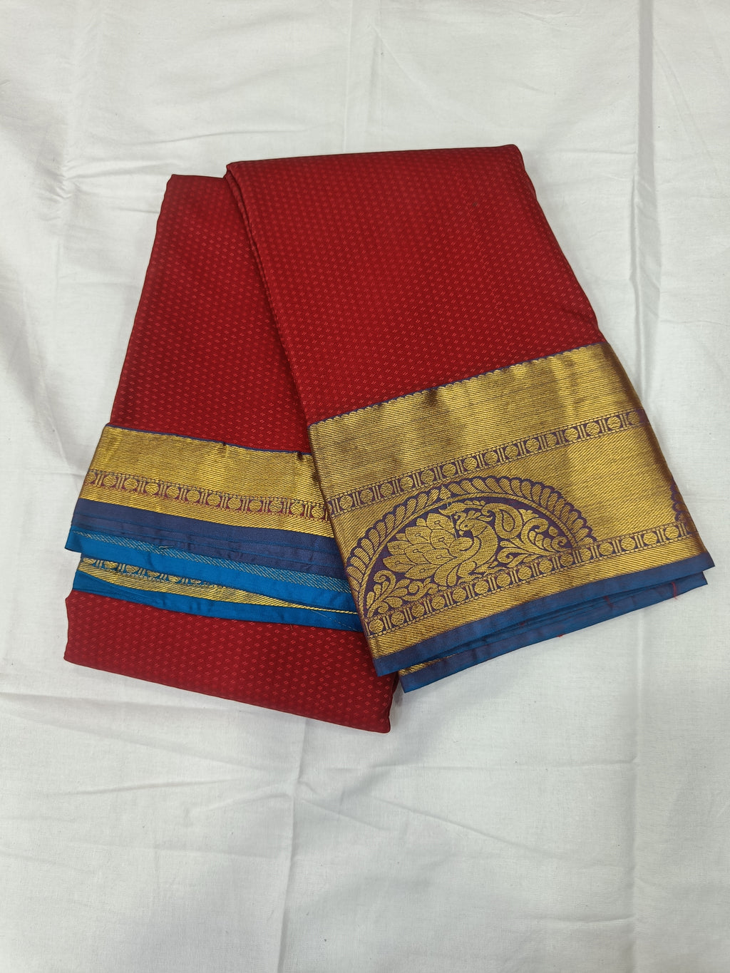 Red silk saree with blue accent border, gold hem panel, folded view