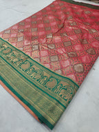 Folded pink saree fabric with green-gold border, geometric patterns, and pallu end