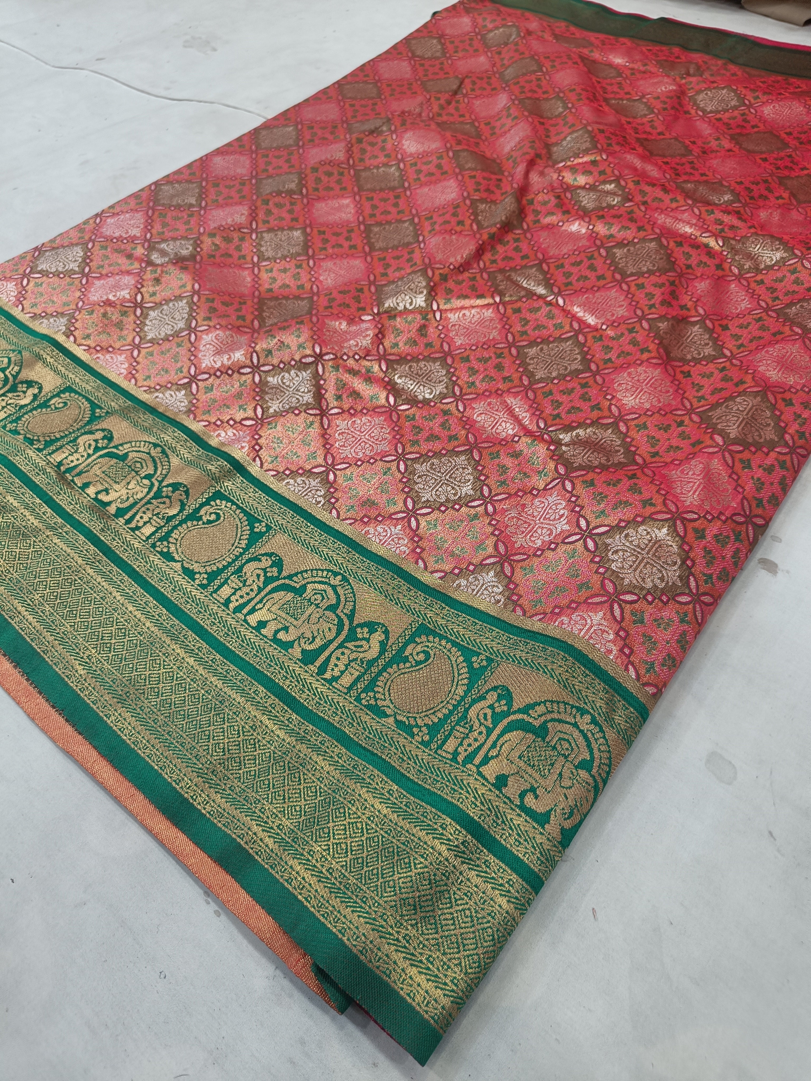 Folded pink saree fabric with green-gold border, geometric patterns, and pallu end