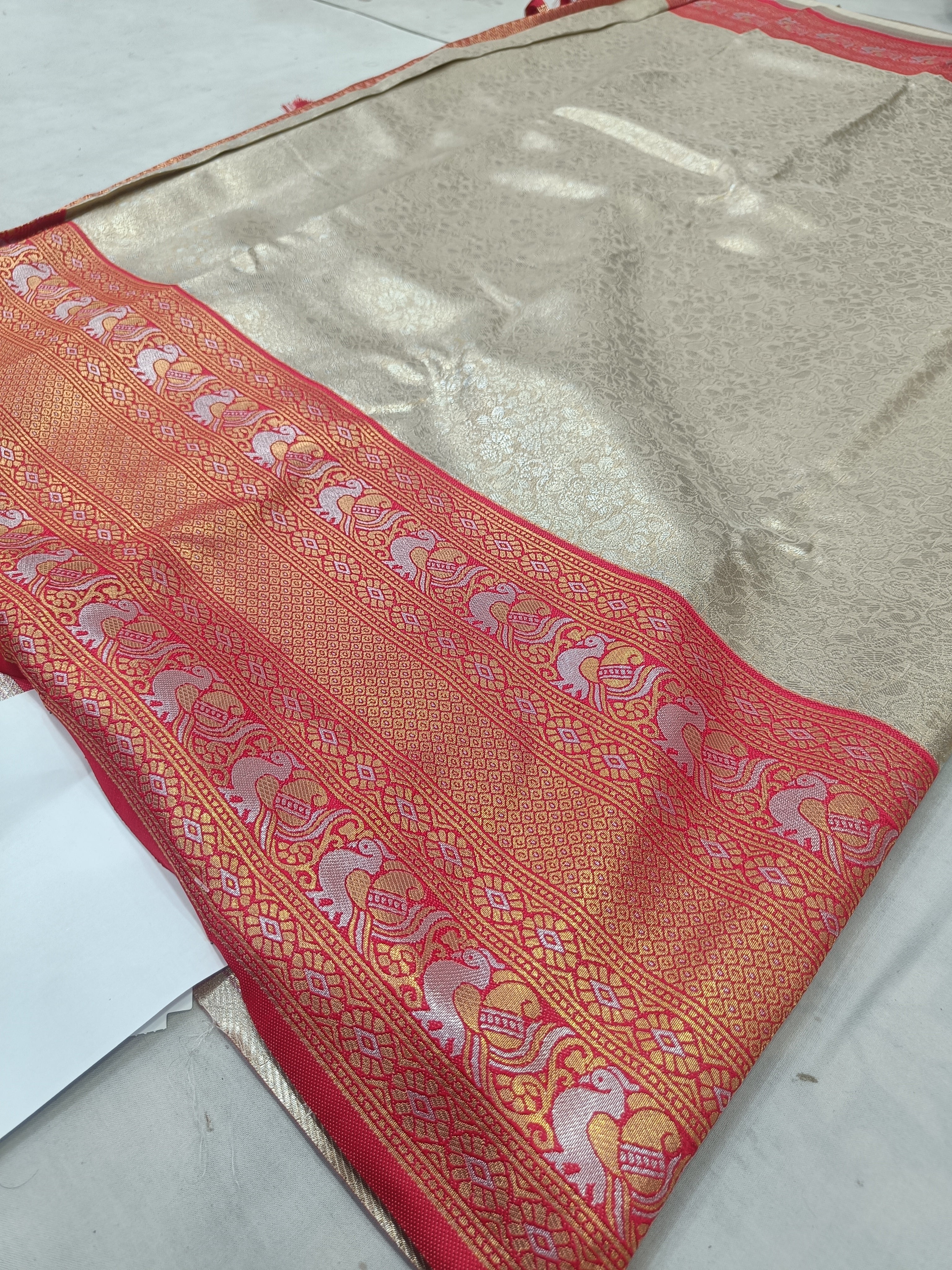 Silver silk saree pallu with red ornate motifs and border, folded on sheet