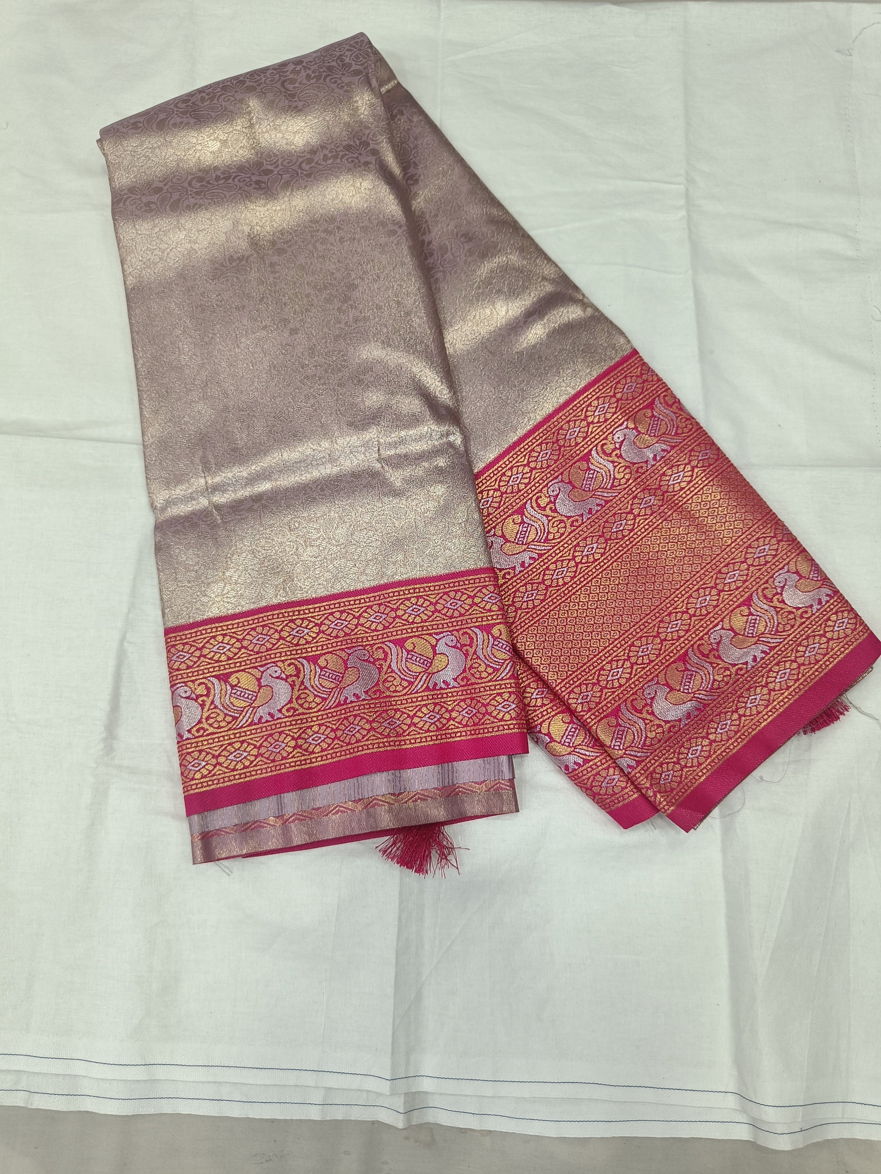 Folded light grey Banarasi silk saree with pink-gold border and matching blouse fabric