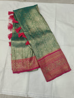 Folded teal green Banarasi silk saree with pink border, tassels, and patterned pallu