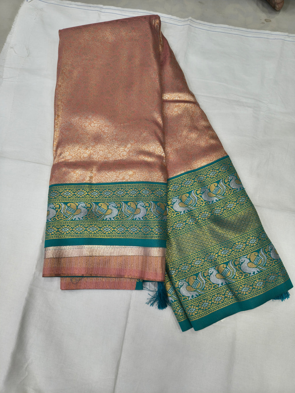 Folded peach silk saree with wide aqua blue border and gold woven motifs
