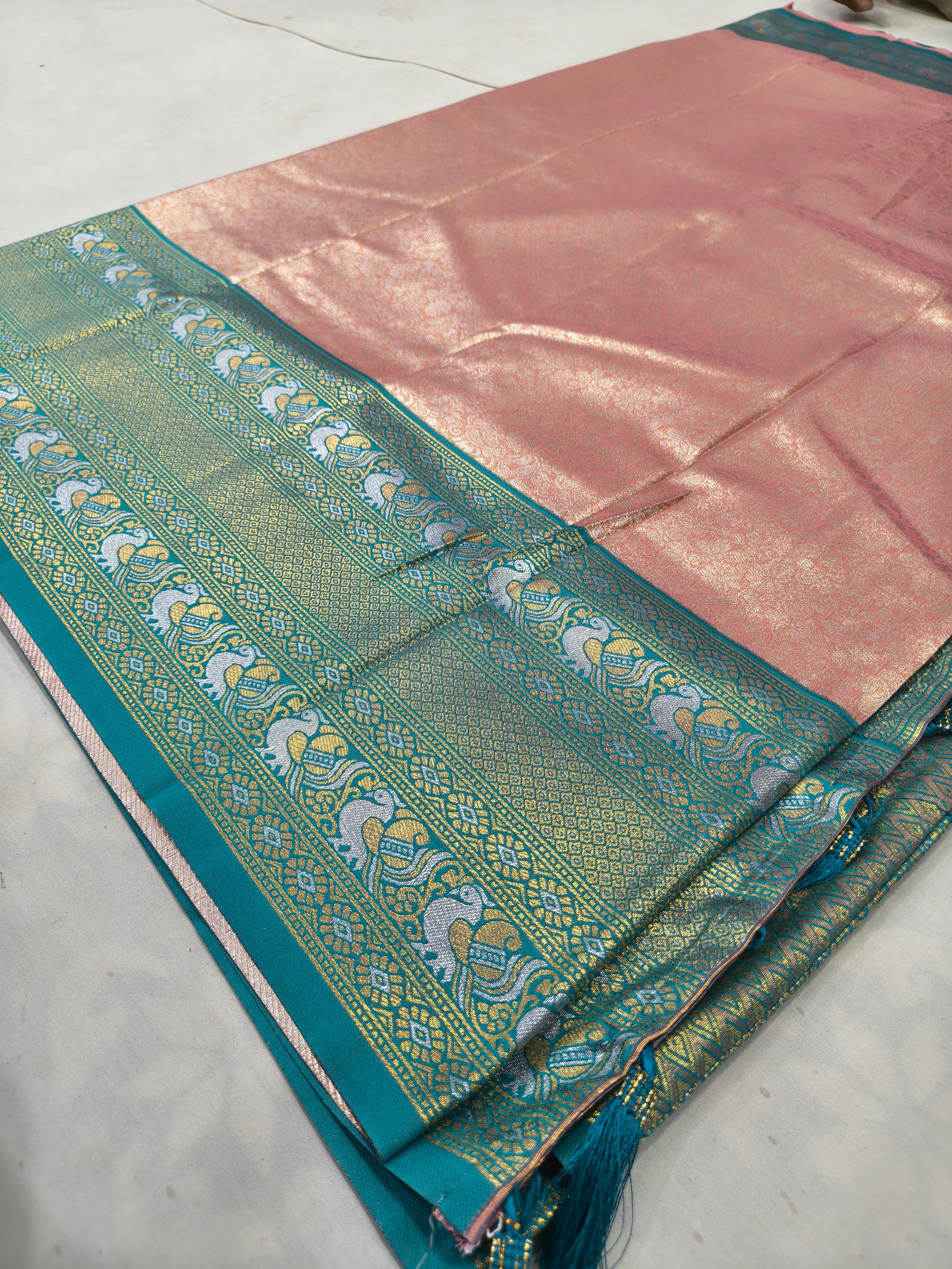 Folded peach silk saree with aqua blue ornamental border and gold woven motifs