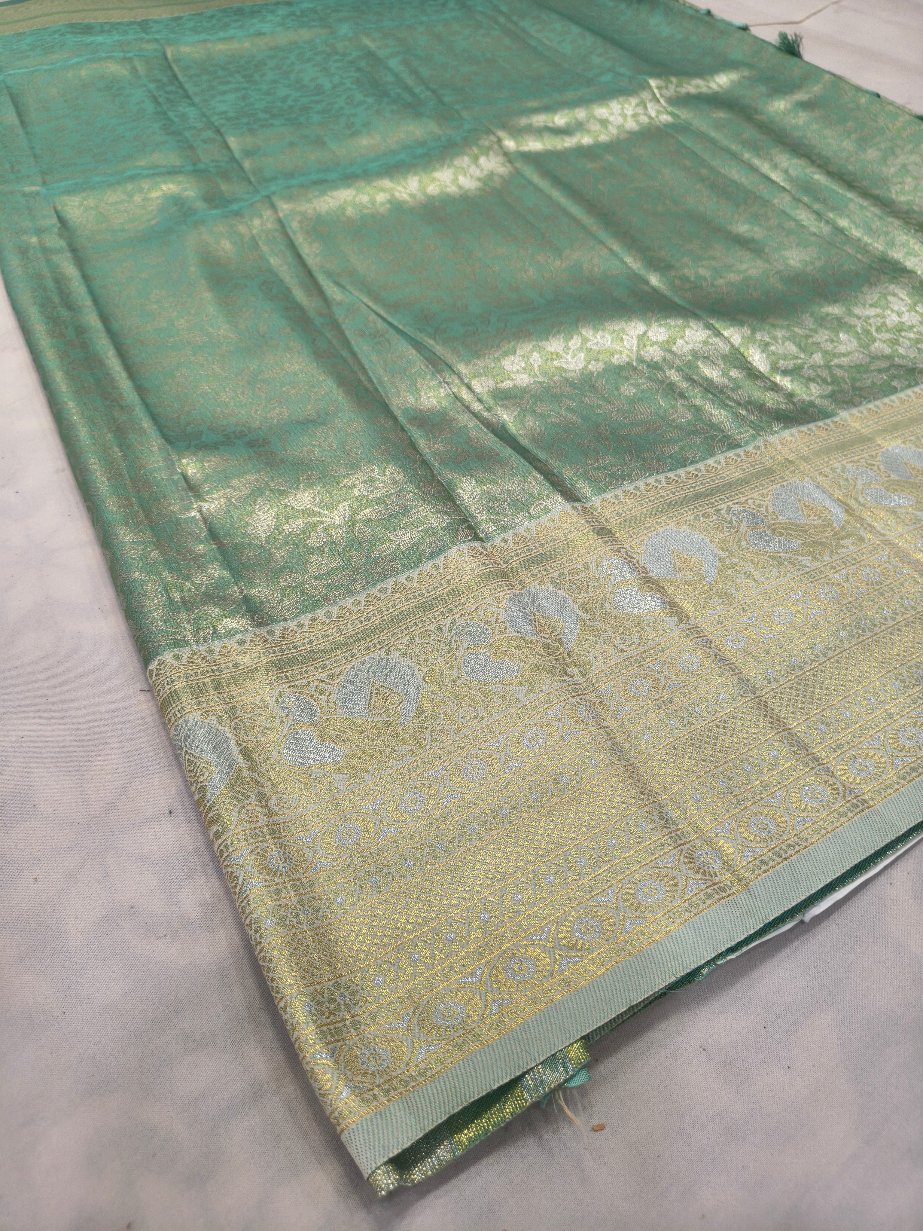 Sea green Banarasi silk saree laid flat with beige zari border and tassel fringe