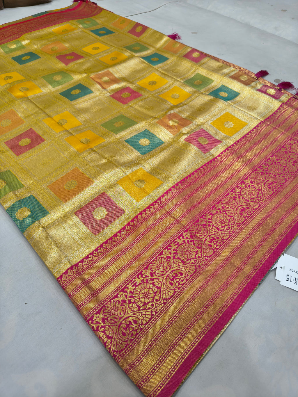 Banarasi silk saree with yellow square pattern, pink-red border, and tassel trim