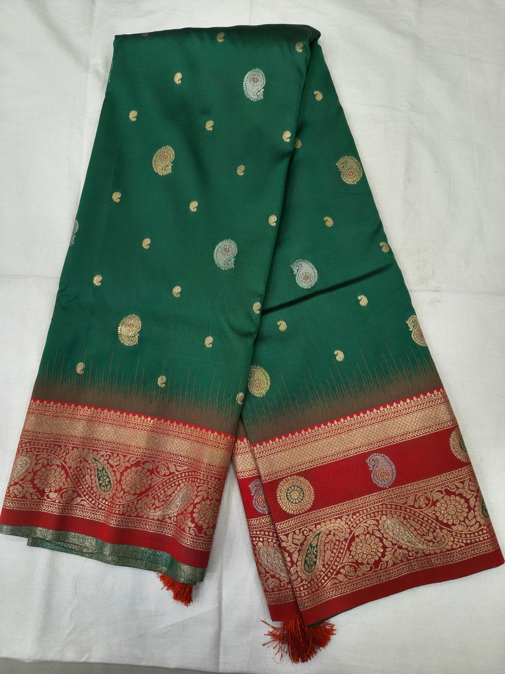Teal green silk saree folded flat with small gold motifs and red patterned border