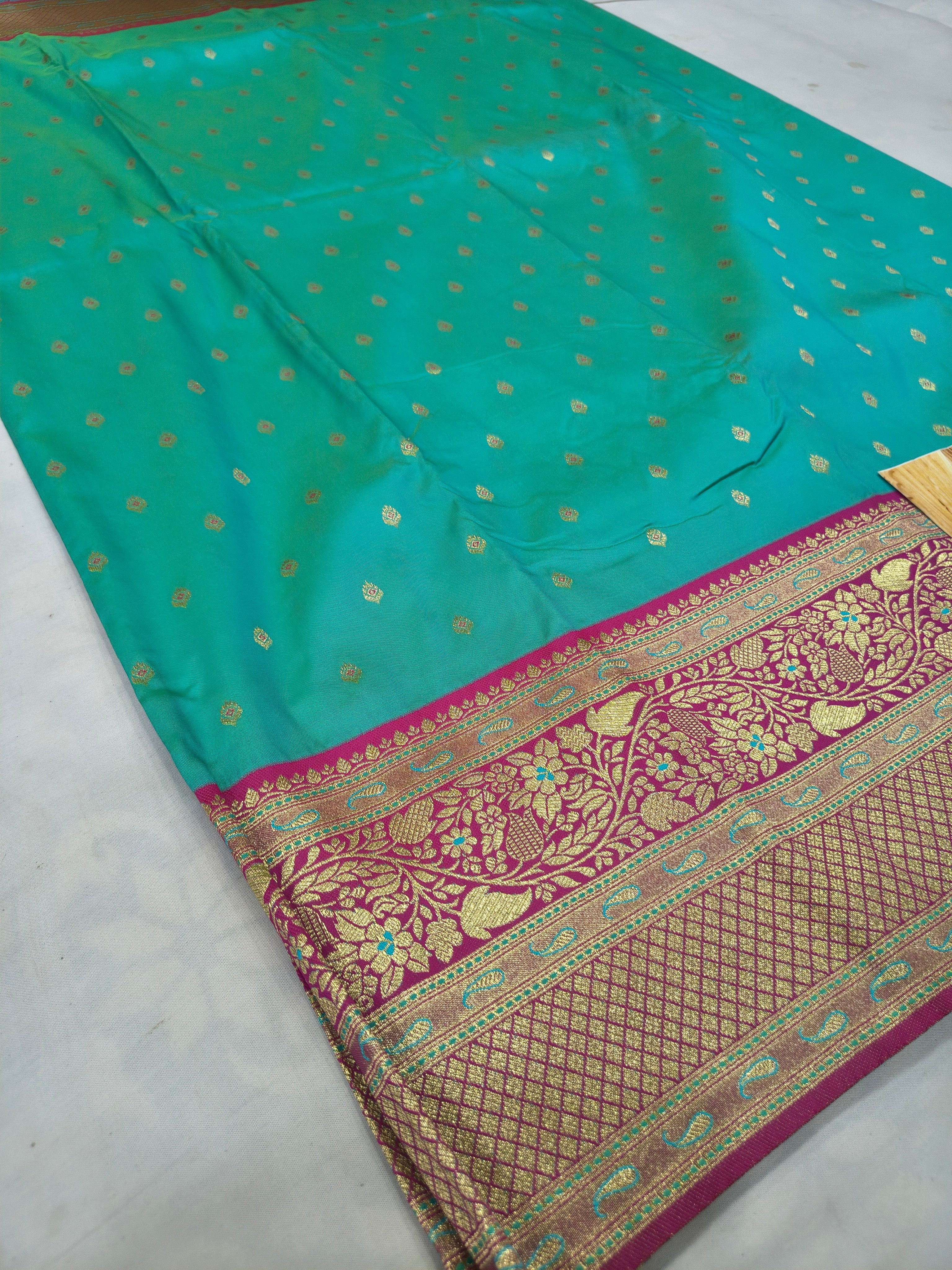 Folded turquoise Banarasi silk saree with gold motifs and maroon-gold border