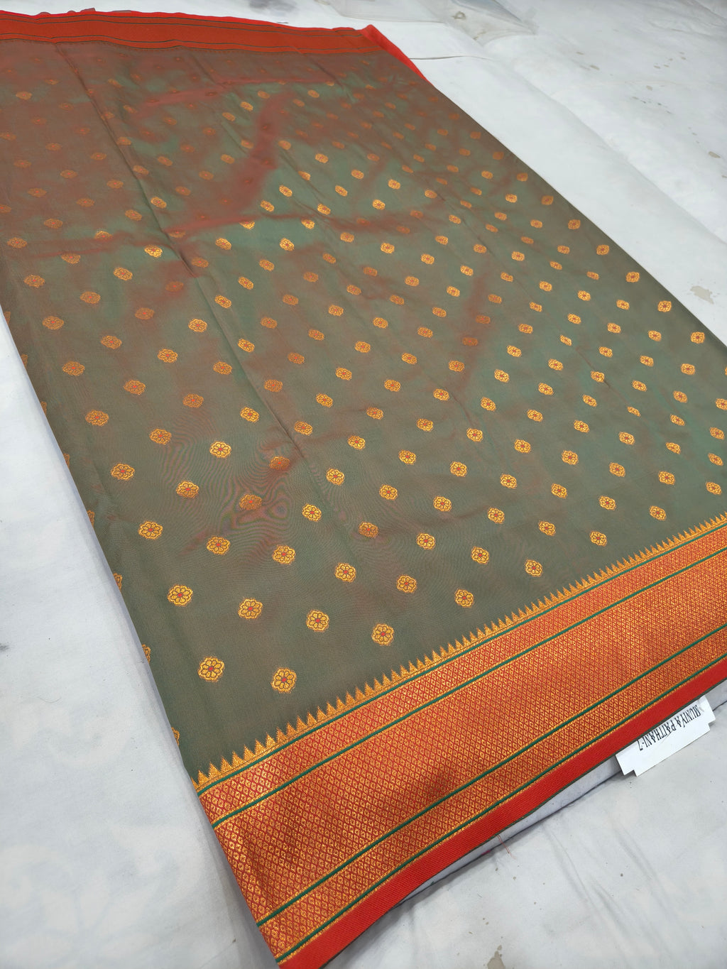 Grey-green silk saree with orange border stripe and small gold motif pattern at edge