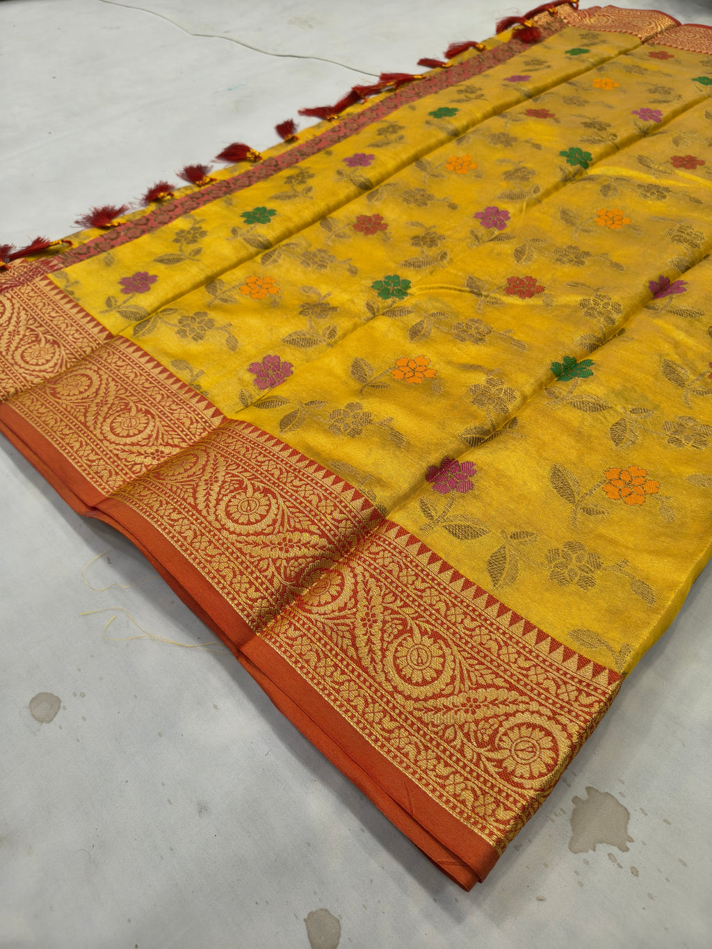 Folded mustard yellow silk saree with floral prints, red woven border and tassels