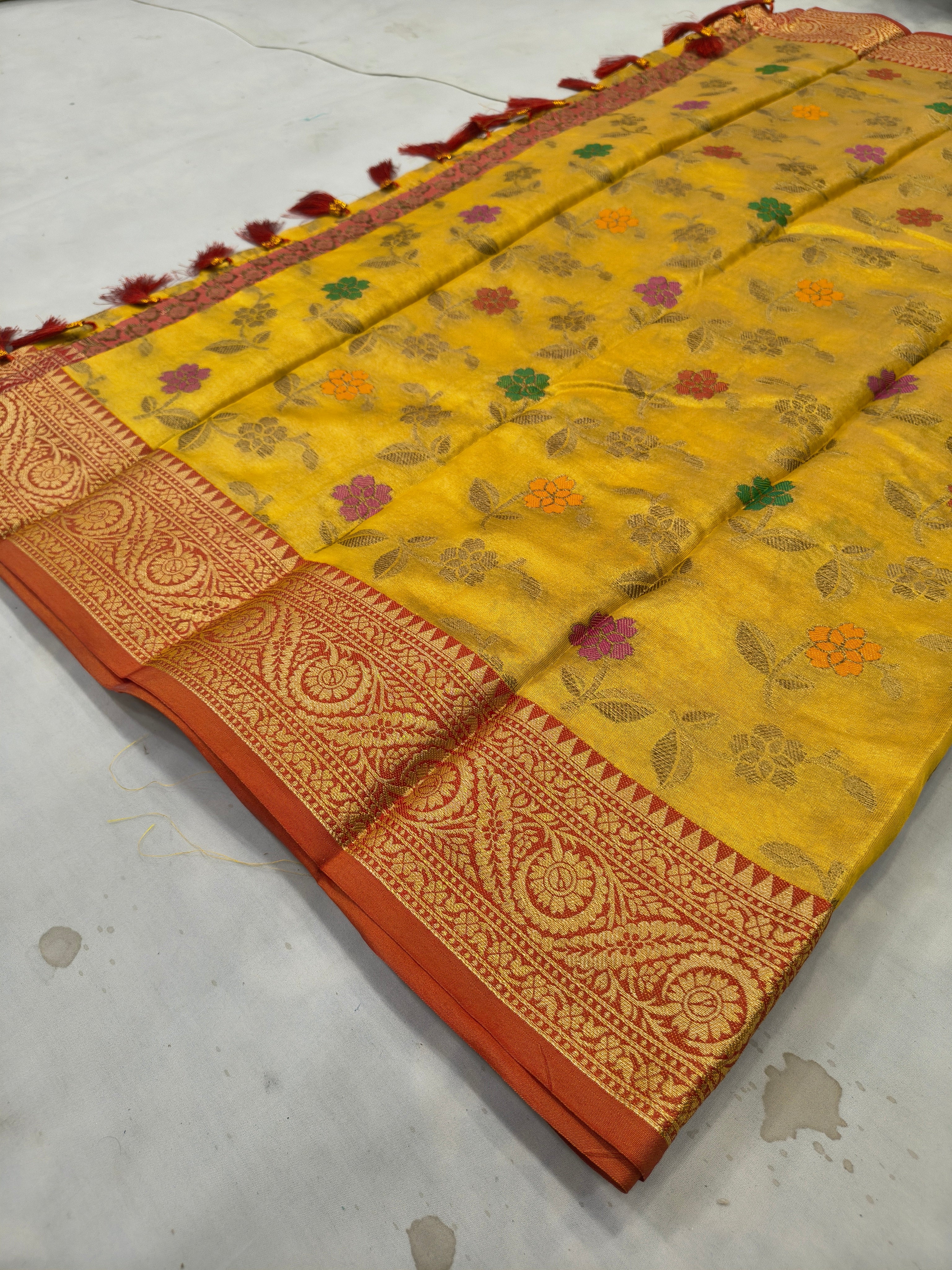 Folded mustard yellow silk saree with floral prints, red woven border and tassels