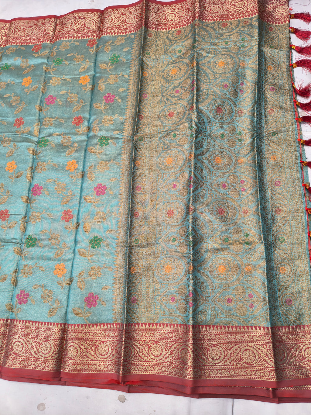 Sky-blue silk saree with floral vine pattern and red-gold border, pleated detail