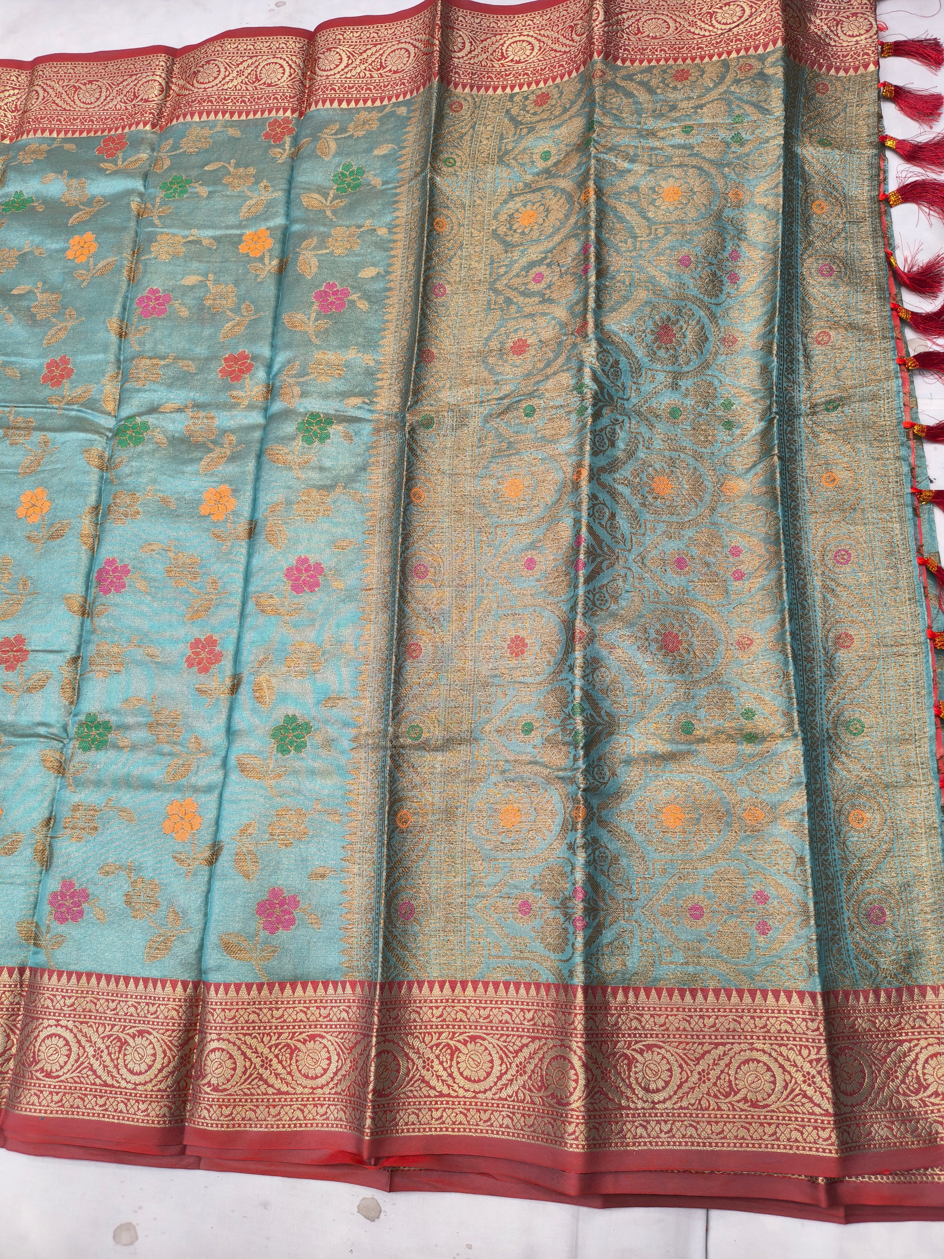 Sky-blue silk saree with floral vine pattern and red-gold border, pleated detail