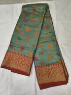 Turquoise silk saree with multicolor leaf print and red-gold woven border, folded