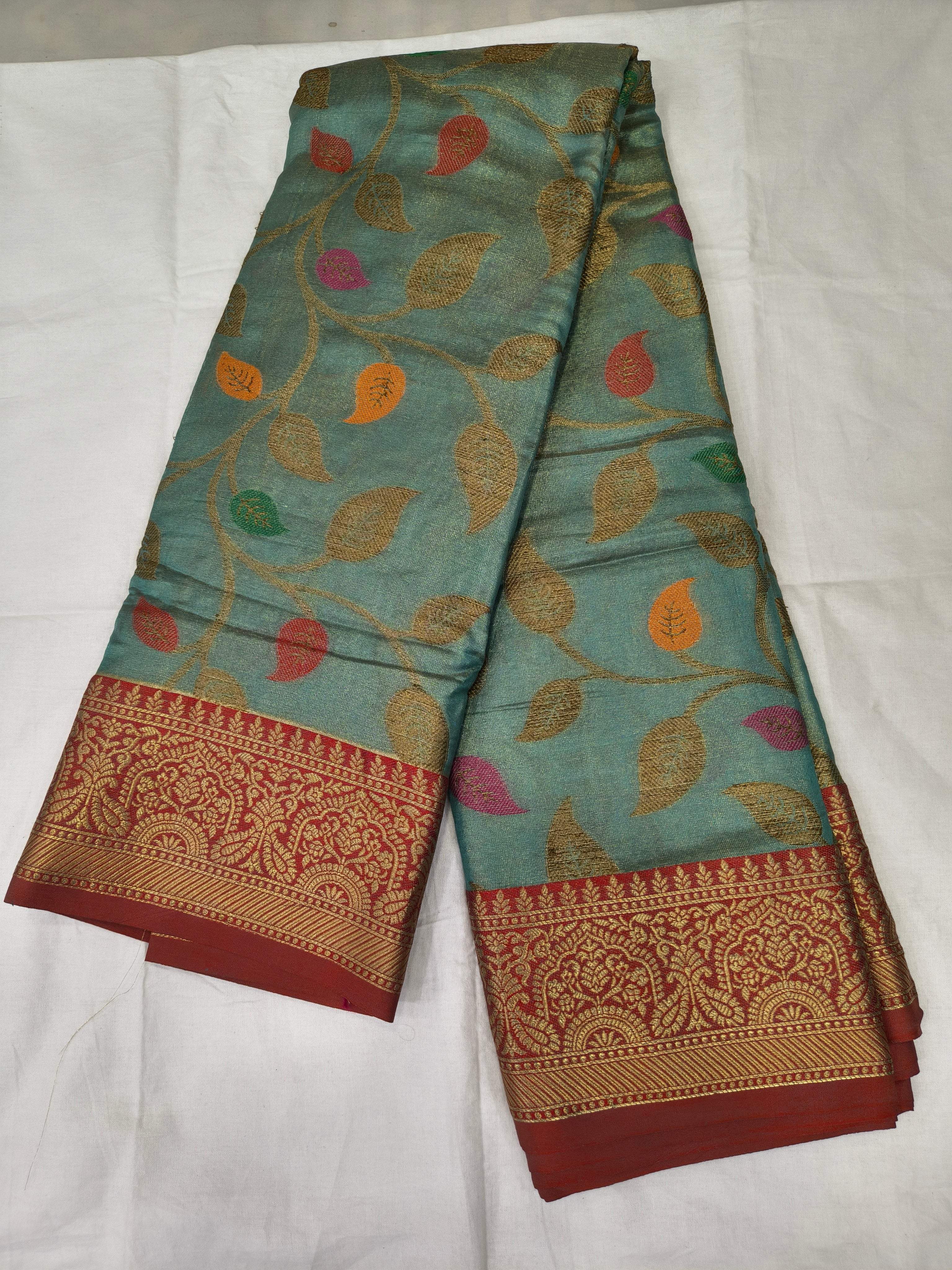 Turquoise silk saree with multicolor leaf print and red-gold woven border, folded