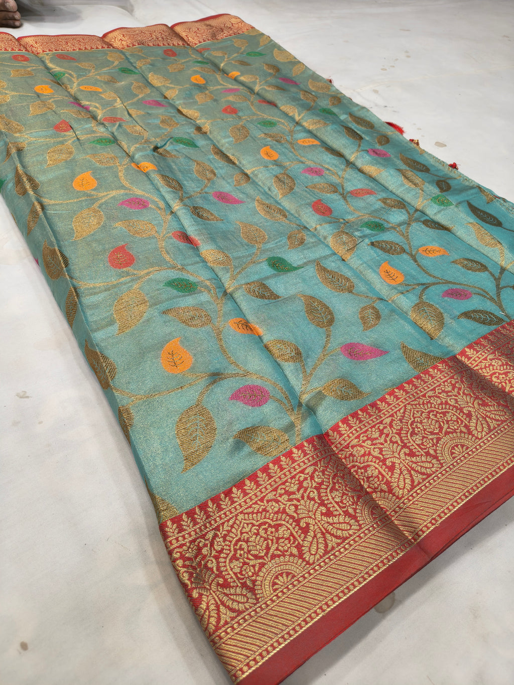 Turquoise silk saree laid flat, leaf motif body with red-gold border