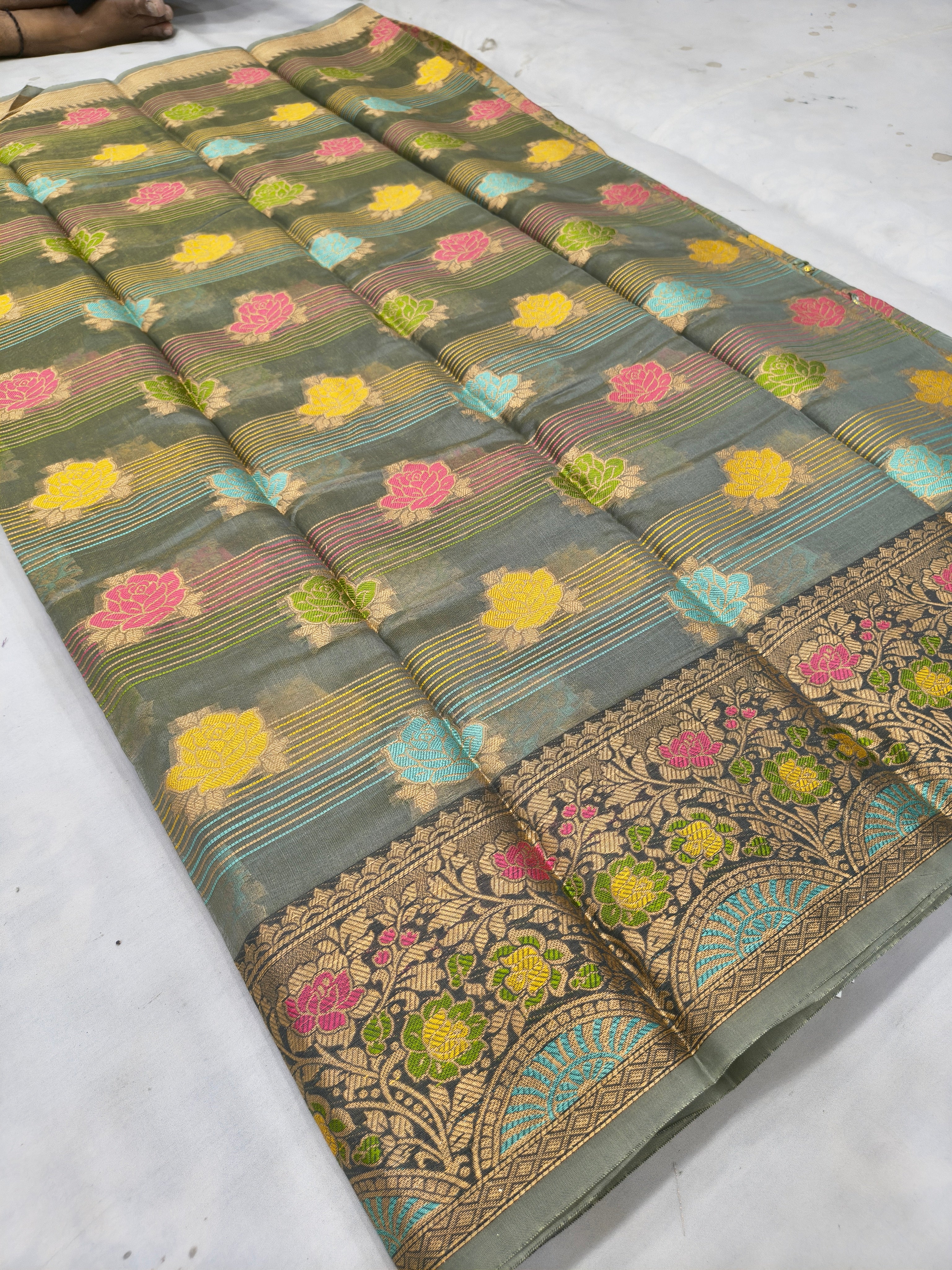 Dark grey silk saree laid flat with colorful flowers, striped bands, and gold border