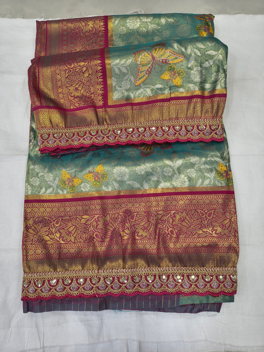 Folded teal-green Banarasi silk saree with pink bands and ornate zari-style border