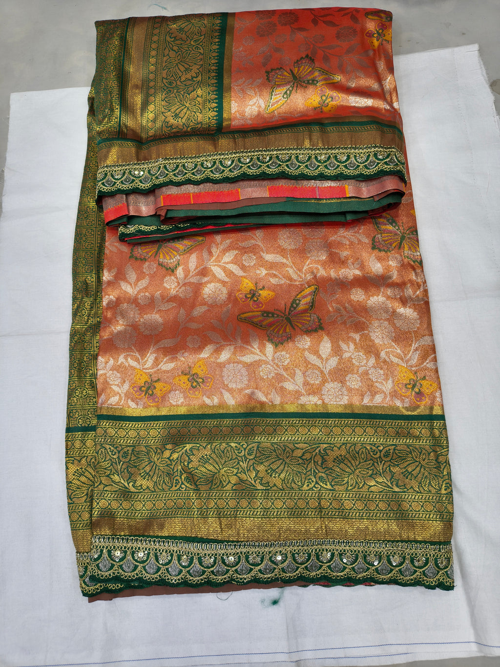 Folded peach and olive Banarasi silk saree with patterned bands and floral prints