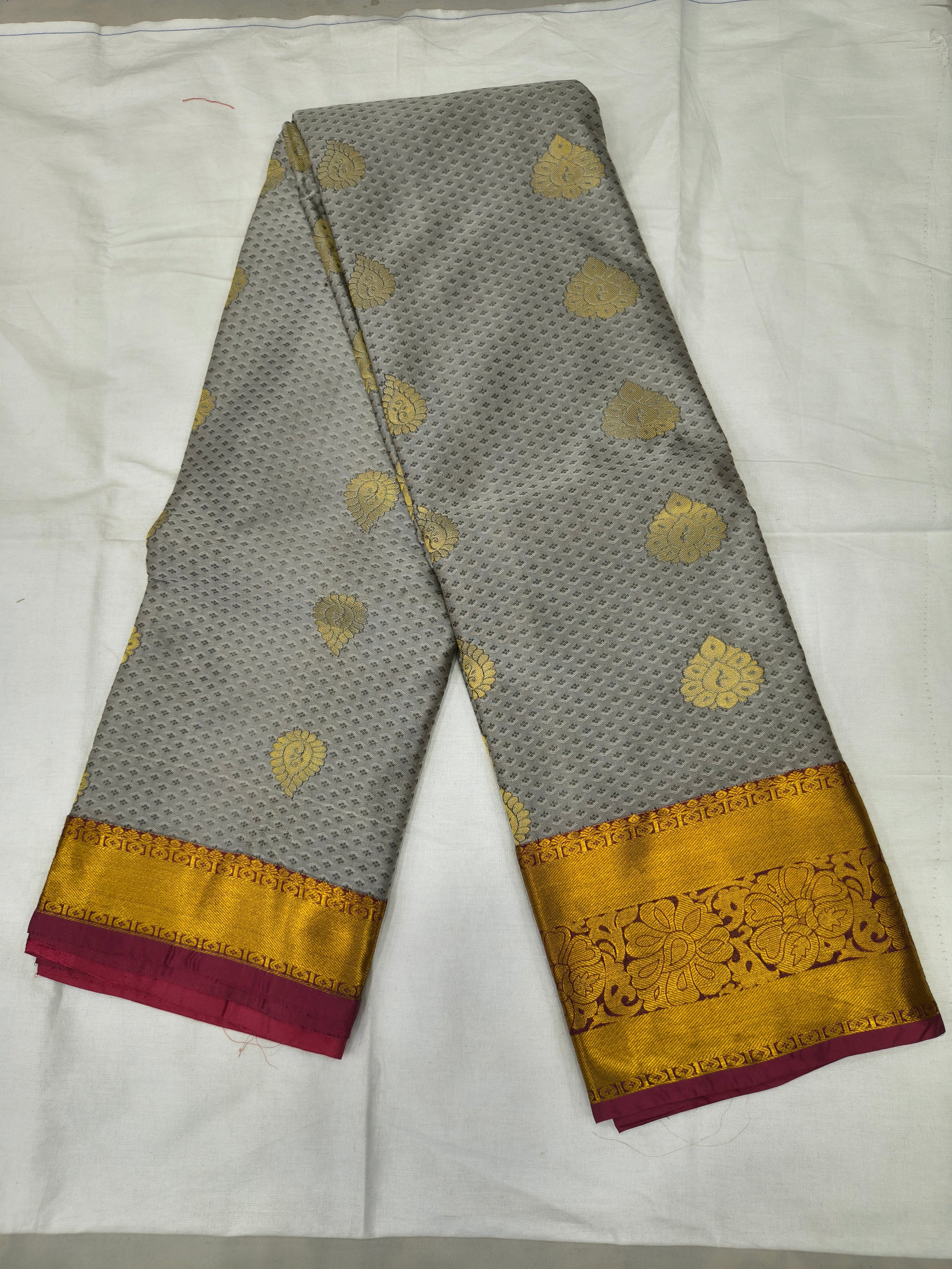 Folded grey saree fabric with small gold motifs, mustard-gold border and red edge