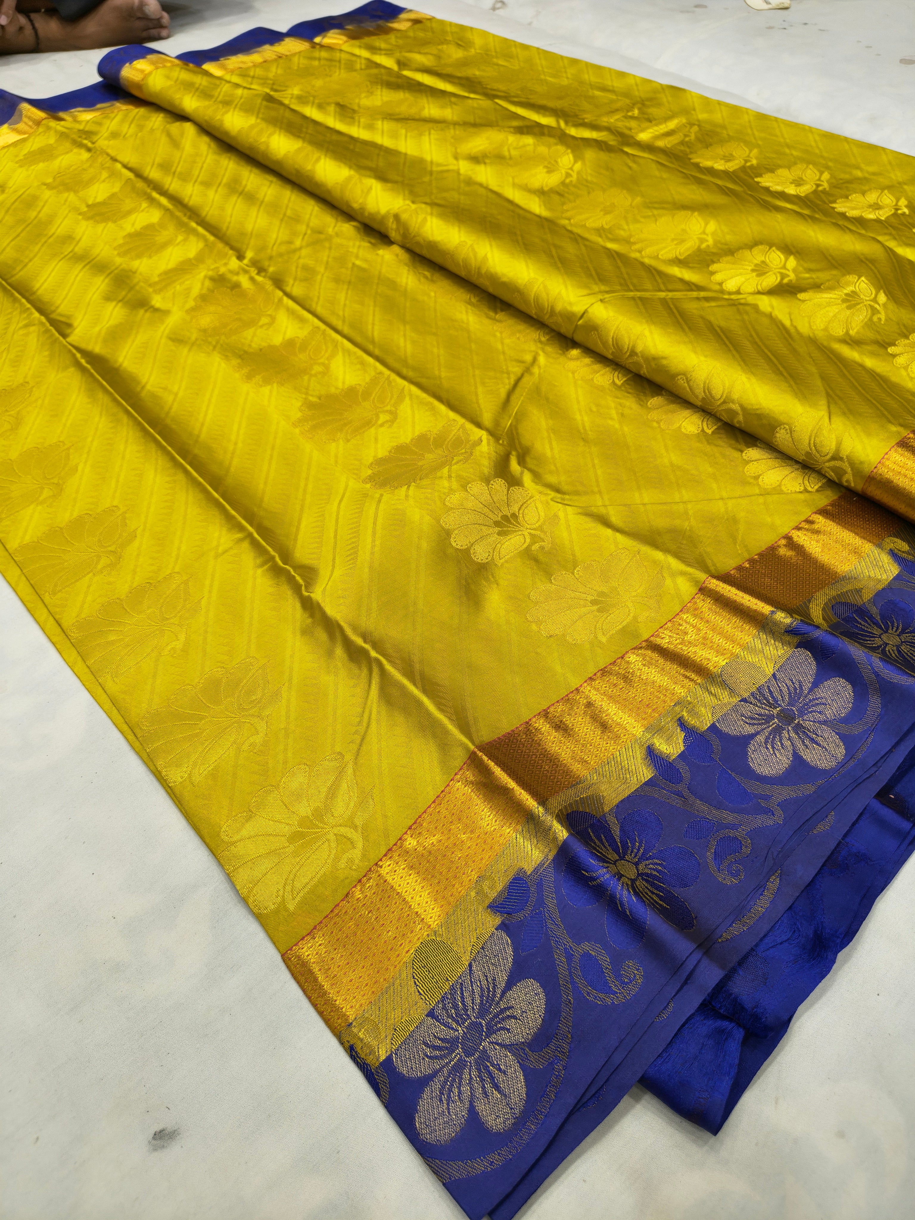 Folded yellow Kanchipuram silk saree with royal blue floral border and gold sheen