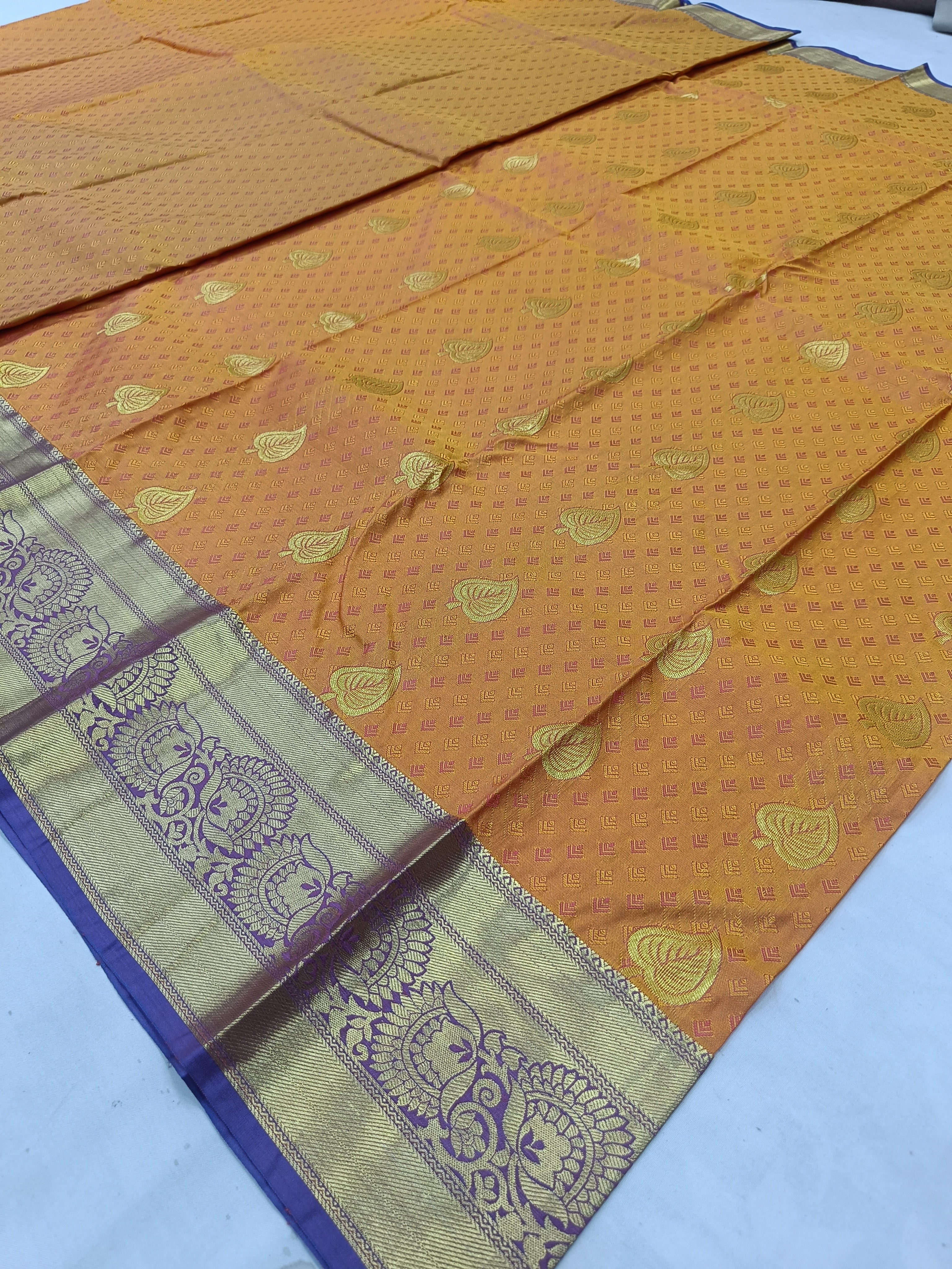 Mustard silk saree with all-over leaf motifs and blue-gold border