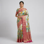 Women's pastel silk saree with teal and green motifs and pink-gold border